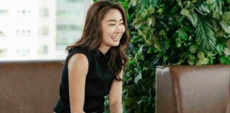 A smiling woman sits in a comfortable, green-filled office environment, surrounded by lush plants that create a relaxing, natural atmosphere. She is holding a pen, appearing engaged and at ease, embodying the spirit of National Wellness Month by highlighting the importance of a healthy and balanced workplace that promotes both mental and physical wellbeing.