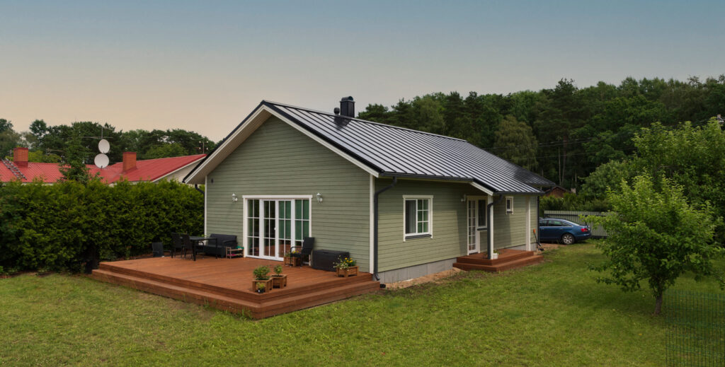 A cosy wooden house with a sleek black solar roof surrounded by trees and a lush lawn.