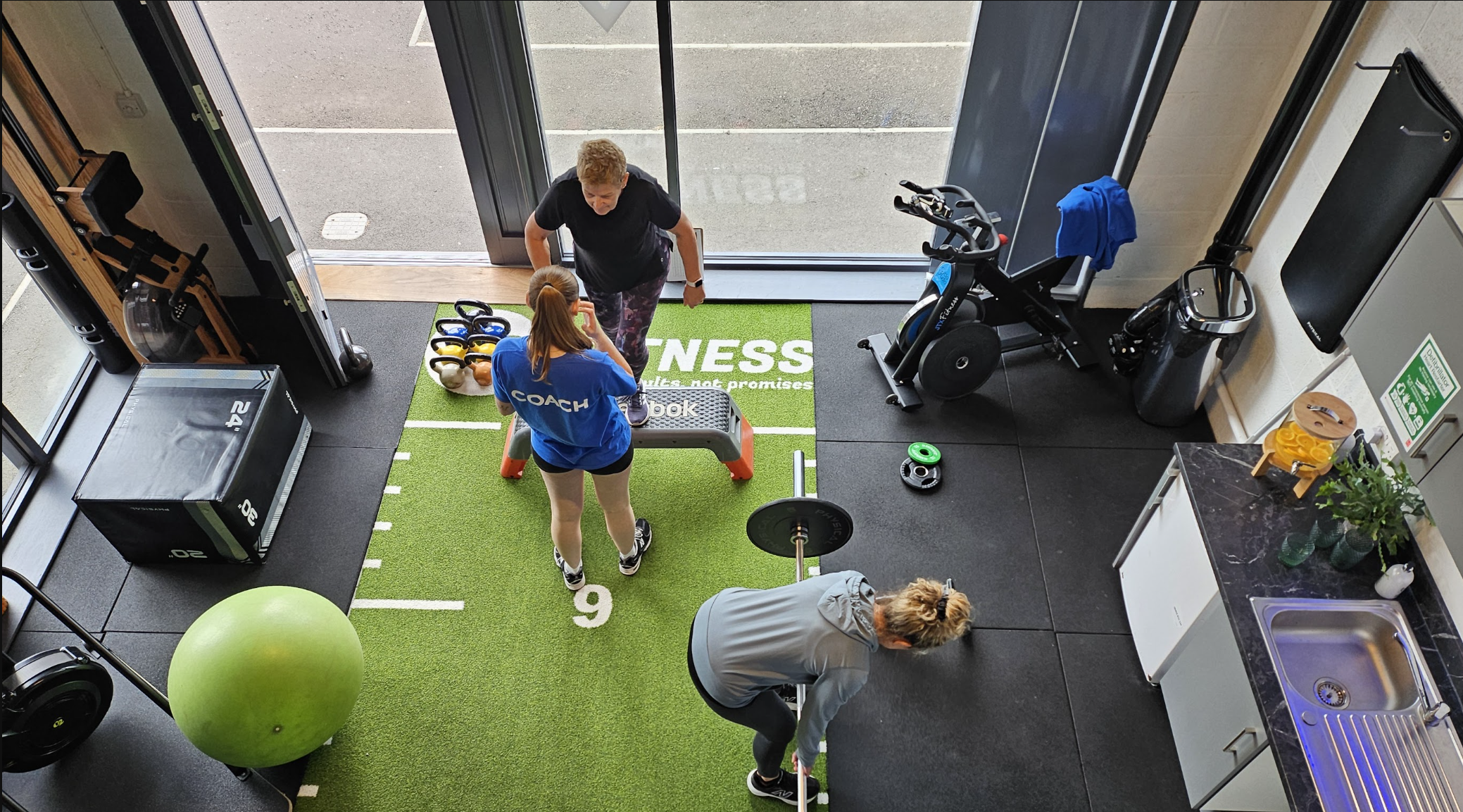 A birds eye view of Go Fitness gym, showing the coach coaching a client on step ups with another member working out on the side.