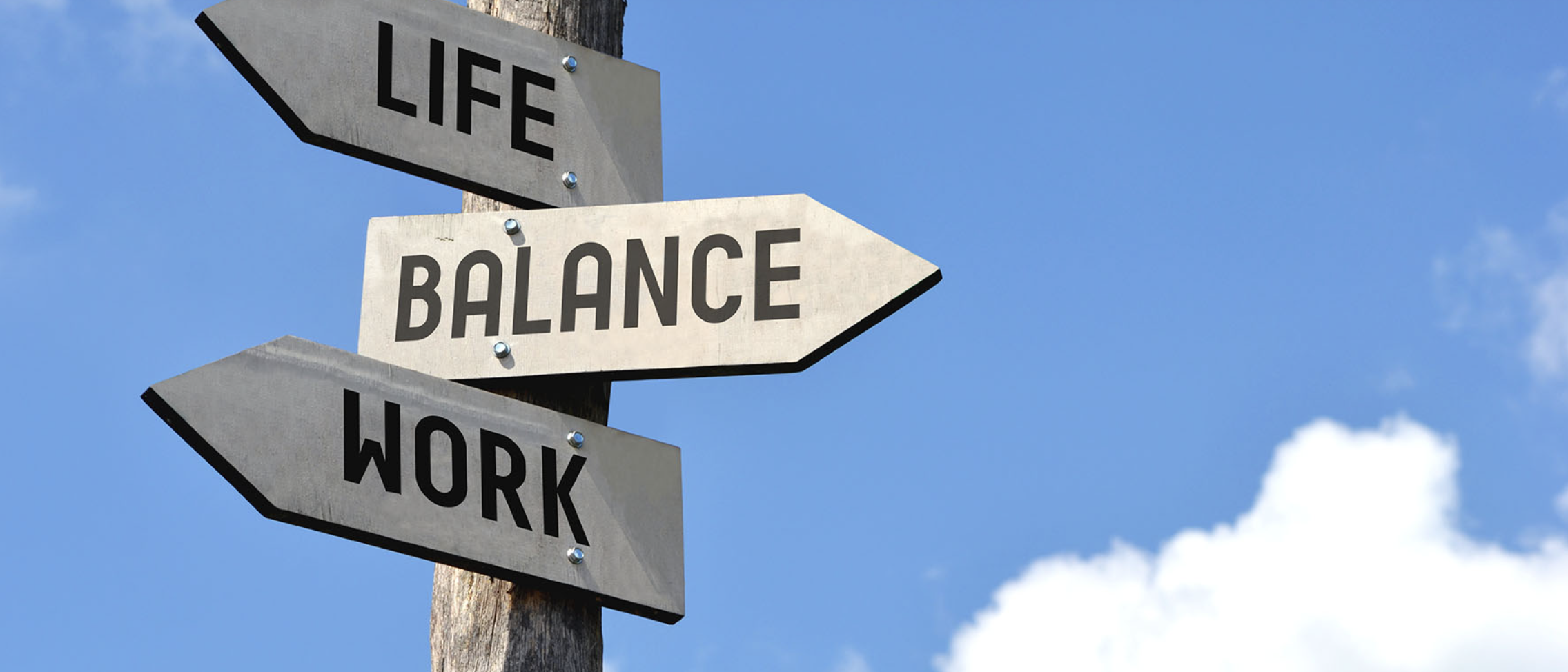 A photo with a sign post with posts show casing life, balance and work with a sky as the background