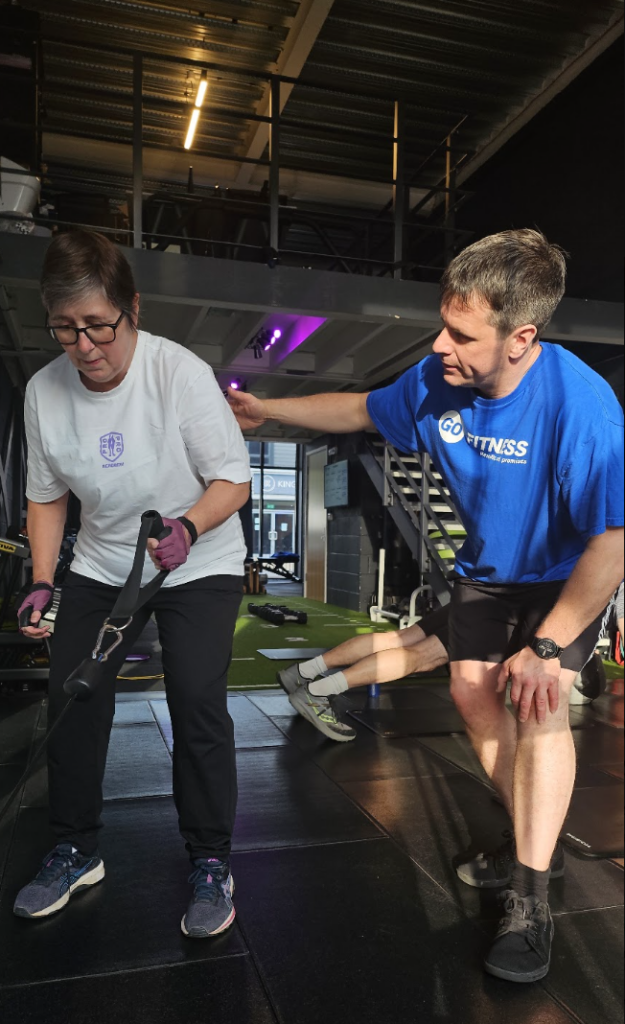 Here is a photo of a Personal trainer coaching a client, being up close and personal to make sure they've got the right form for a cable row. 